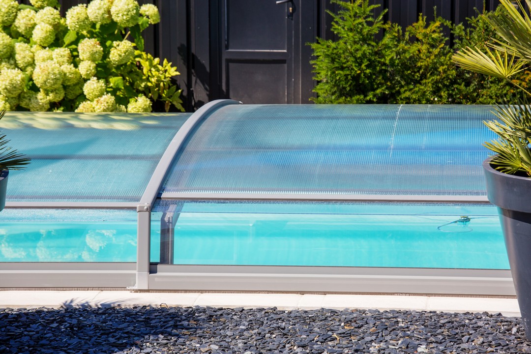 Un abri bas rectangulaire recouvre une piscine.